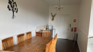 A dining area with a wooden table and chairs, a kitchen in the background, and a deer head decoration on the wall. - Library Cottage (Hamilton)