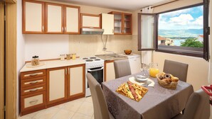 A compact kitchen with wooden cabinets, a stove, and a dining table set for breakfast. - Sun Spalato Villa Alisa (Mastrinka)