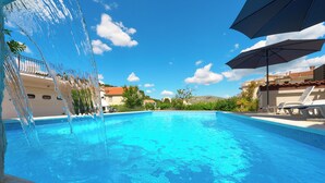 A swimming pool with clear blue water, a water fountain, and a large umbrella providing shade. - Sun Spalato Villa Alisa (Mastrinka)