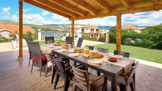 An outdoor dining area with a wooden pergola, a table set for a meal, and a view of houses and hills in the background. - Sun Spalato Villa Alisa (Mastrinka)