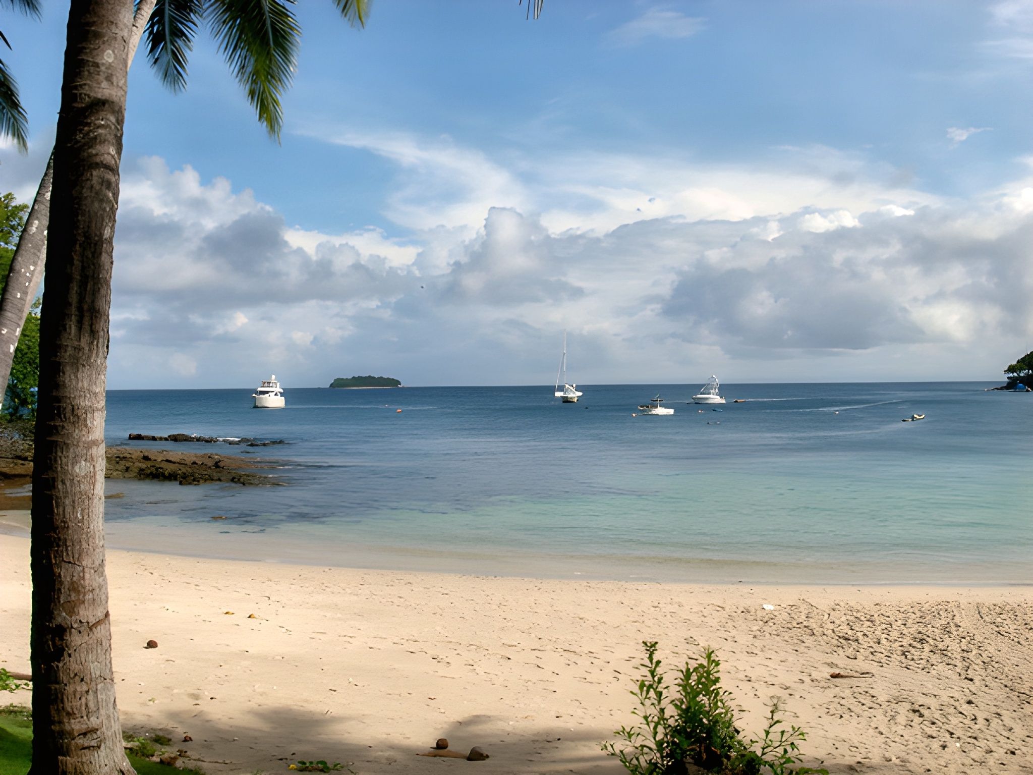 A beach with clear water, boats, and a distant island.