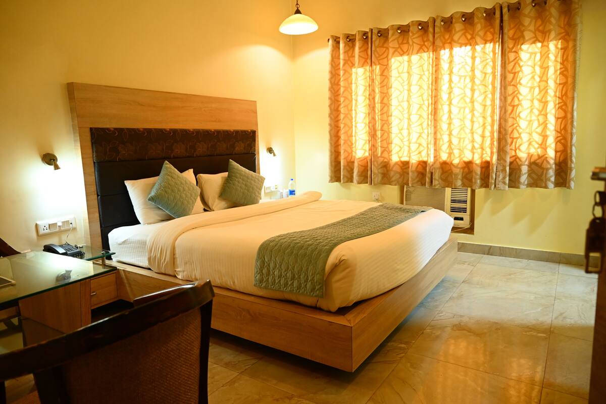 A neatly made bed with a wooden headboard, a bedside table with a lamp, and a window with patterned curtains.