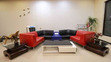 A modern waiting area with a red and black sofa set, a glass coffee table, and a small side table with a plant.