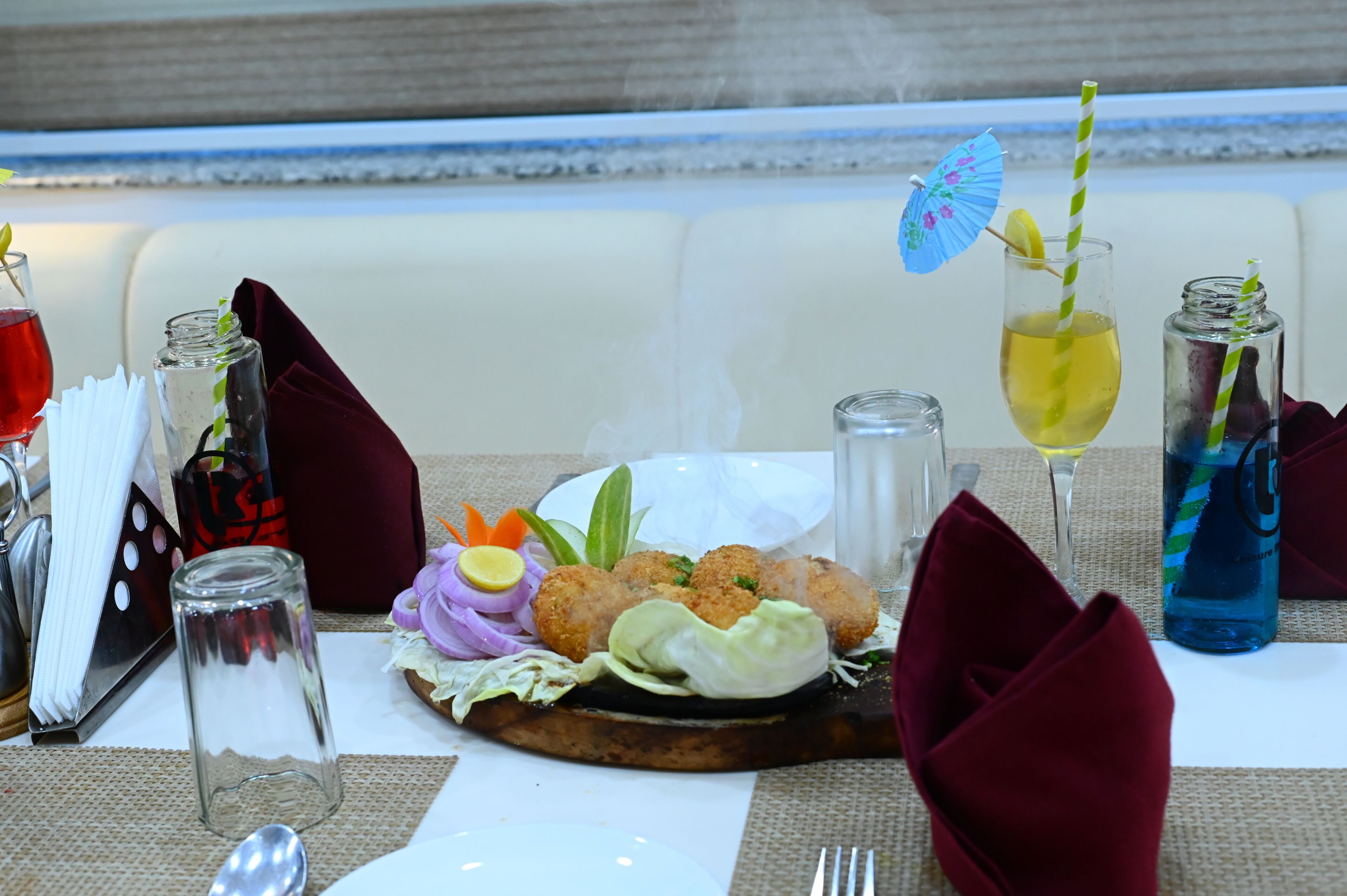 A table set with a meal, including a salad, bread, and drinks, with a view of the sea in the background.