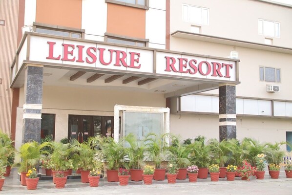 A building with a sign reading "LEISURE RESORT" above the entrance, surrounded by potted plants.