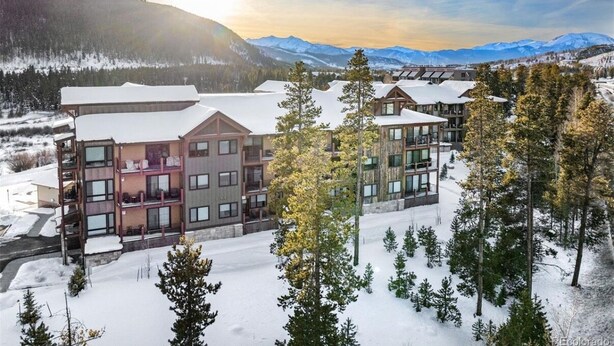 A multi-story hotel with a modern design, featuring large windows and a snow-covered landscape with mountains in the background.