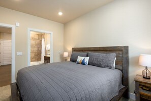 Un dormitorio con una cama grande, cabecera de madera, dos lámparas de noche y un baño visible a través de una puerta abierta.