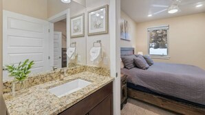 A bedroom with a bed, a nightstand, a vanity with a sink, and a window.