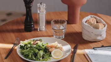 Un repas composé d’une salade et d’un plat de poisson, un verre d’eau, du pain dans un panier et un menu posé sur une table en bois.
