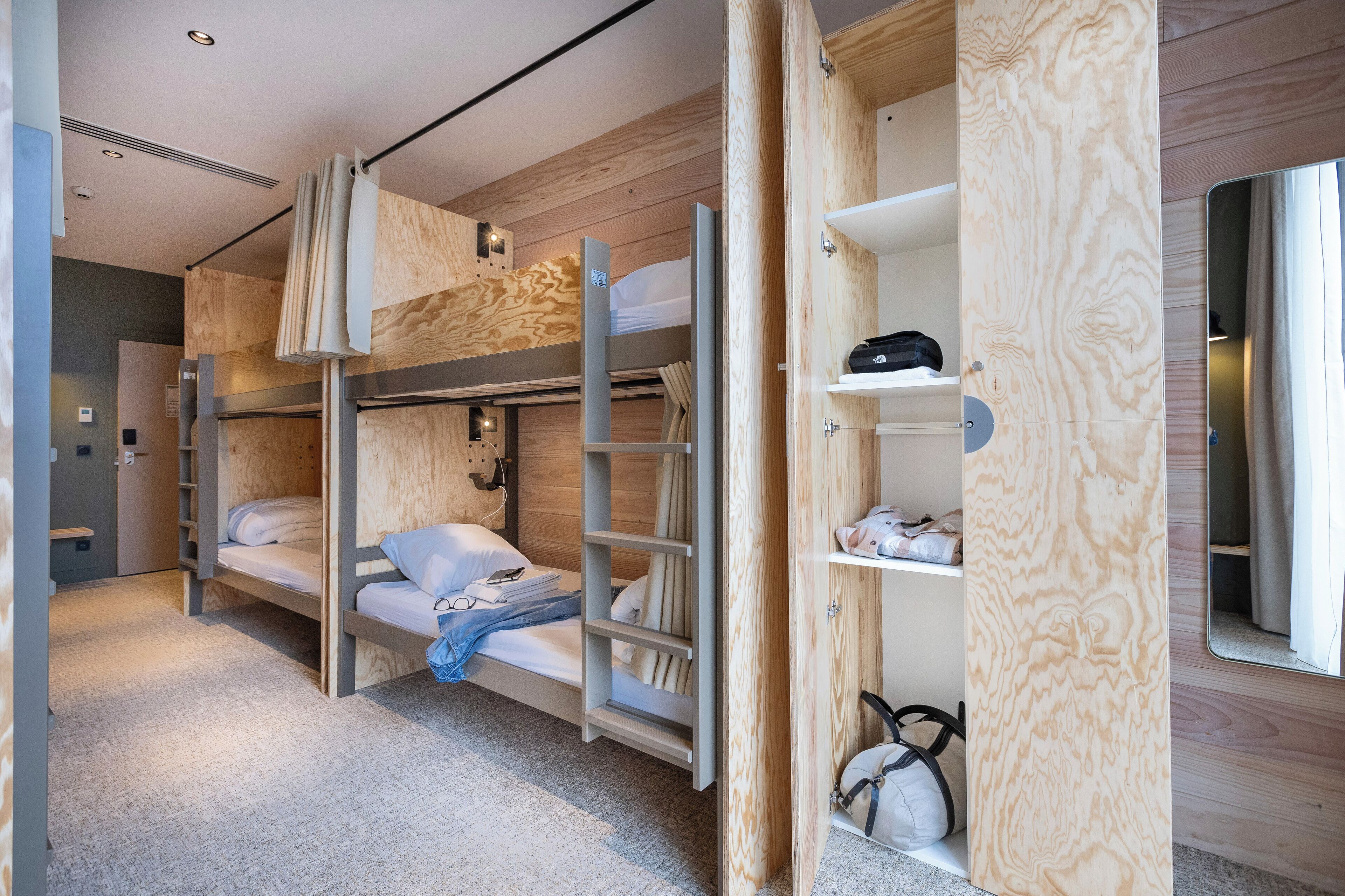 A modern, compact room with bunk beds, a wooden wardrobe, and a mirror.