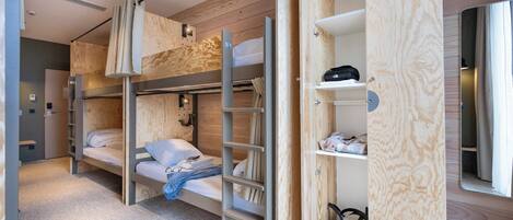 A modern, compact room with bunk beds, a wooden wardrobe, and a mirror.