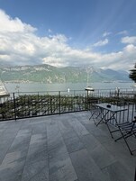 Una terrazza con vista su un lago e montagne, completa di posti a sedere all'aperto e ringhiera.