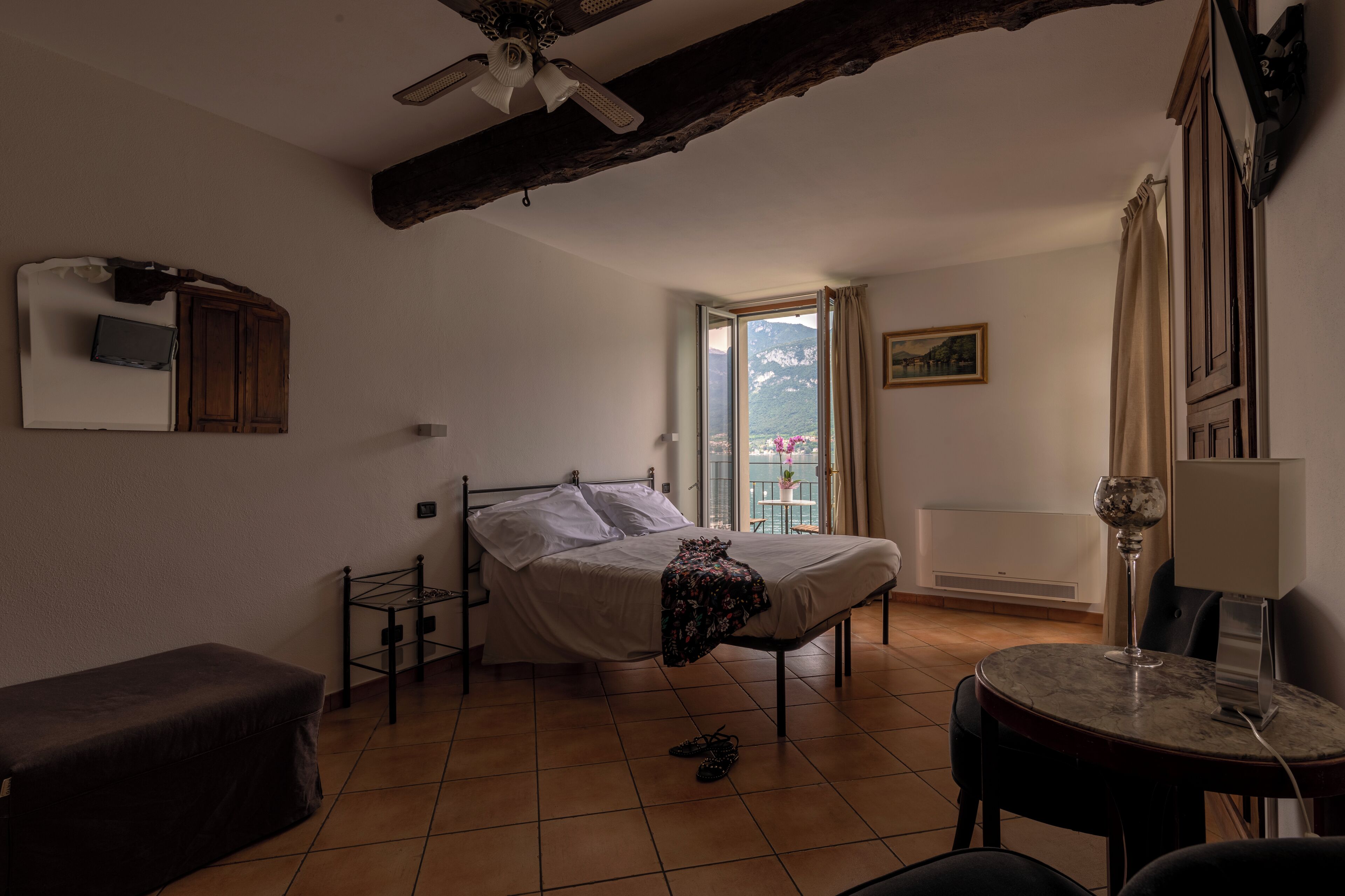 A bedroom with a bed, a small table with a wine glass, a bench, and a view of the outdoors.