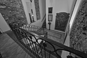 Vista en blanco y negro de una escalera con paredes de piedra, barandillas de metal y obras de arte enmarcadas en las paredes.