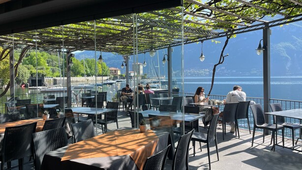 An outdoor cafe with tables and chairs, overlooking a body of water and mountains. - Hotel La Pergola  (Bellagio)