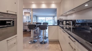 Een moderne keuken met een centraal eiland, barkrukken en uitzicht op een eethoek.