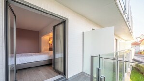 Een modern appartement met een glazen balkon, een bed en een klein zithoekje met een lamp.