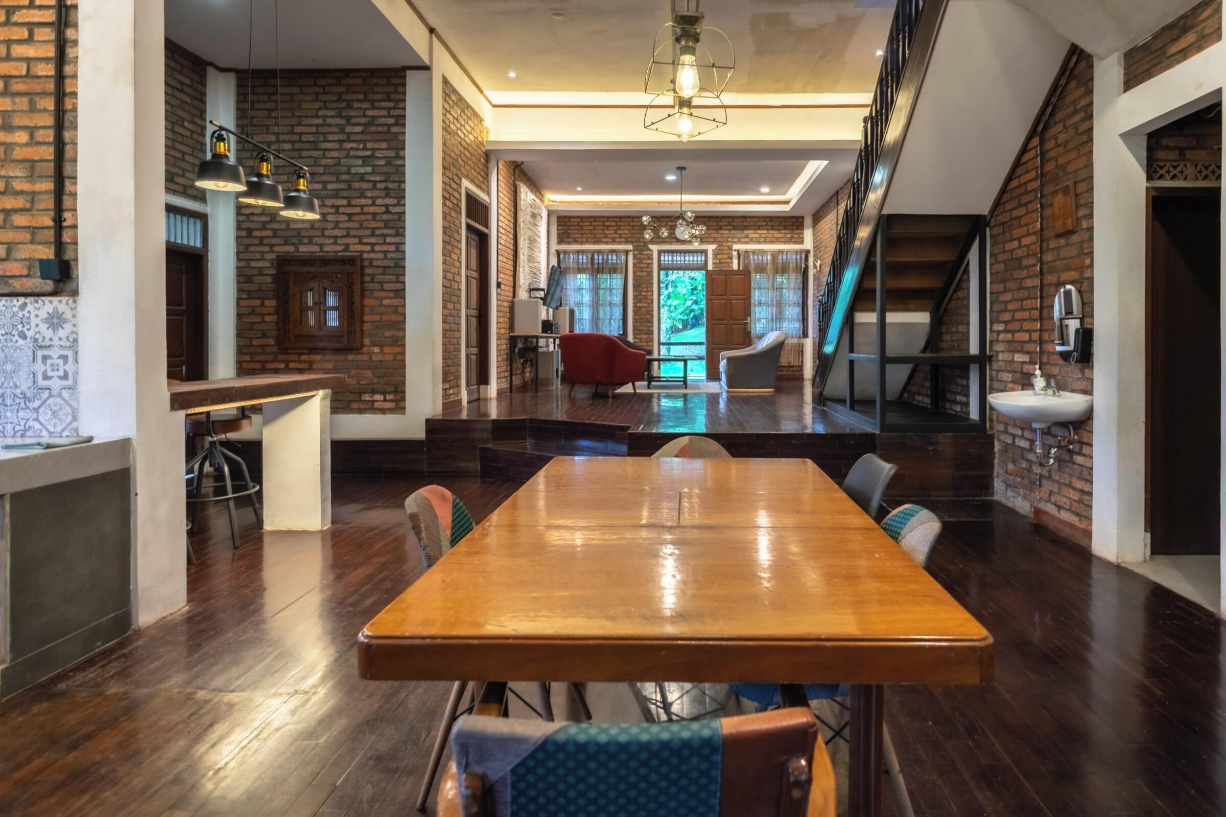 Ein geräumiger Essbereich mit einem langen Holztisch, umgeben von Stühlen, in einem modernen Interieur mit Backsteinwänden und einer Treppe.
