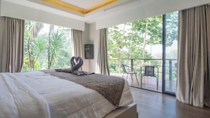 A bedroom with a bed, a balcony with a chair, and a view of greenery. - Lingga Garden House (Cisarua)