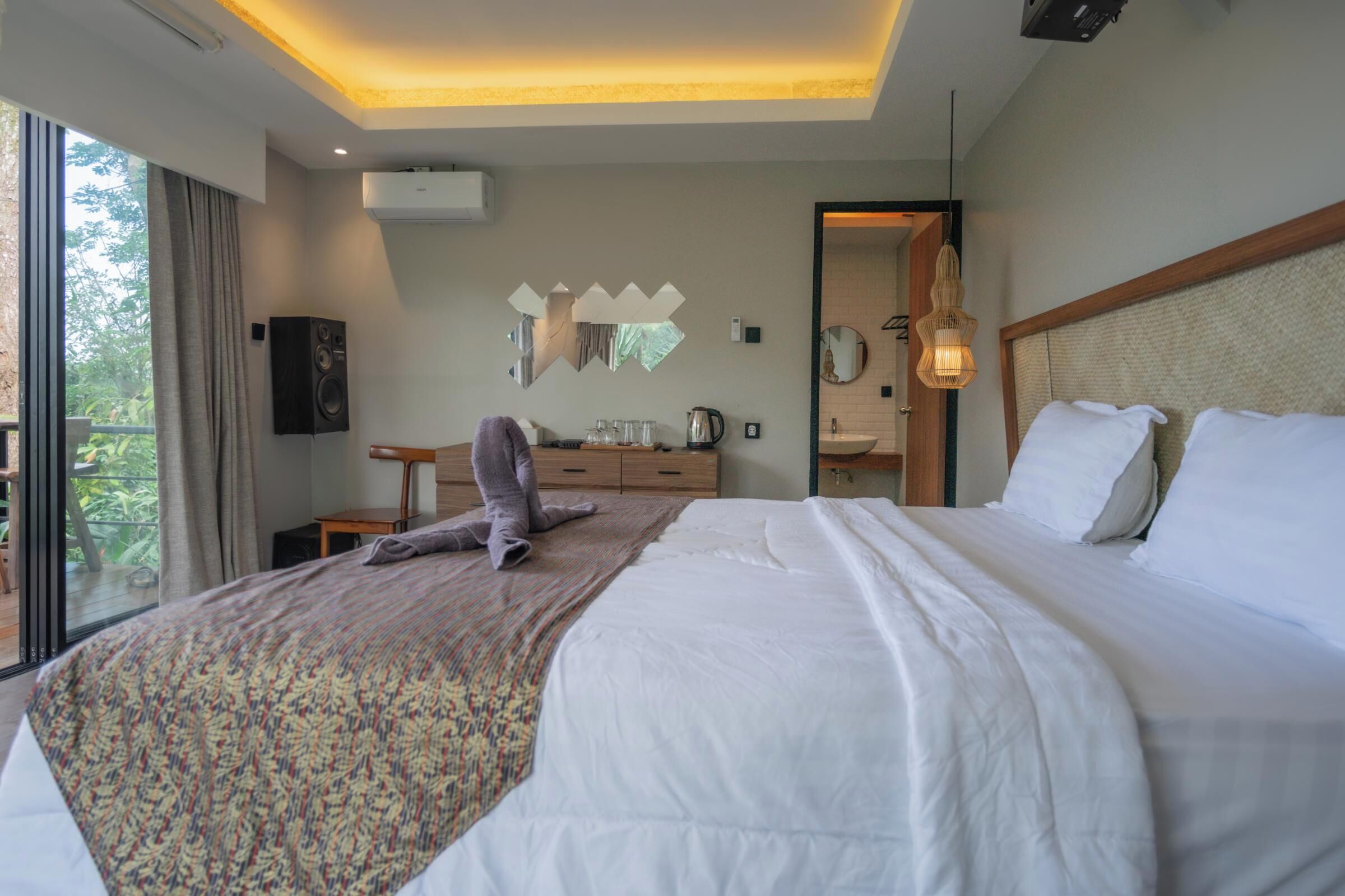 Habitación de hotel moderna con una cama grande, una mesita pequeña, un espejo y vistas al exterior.