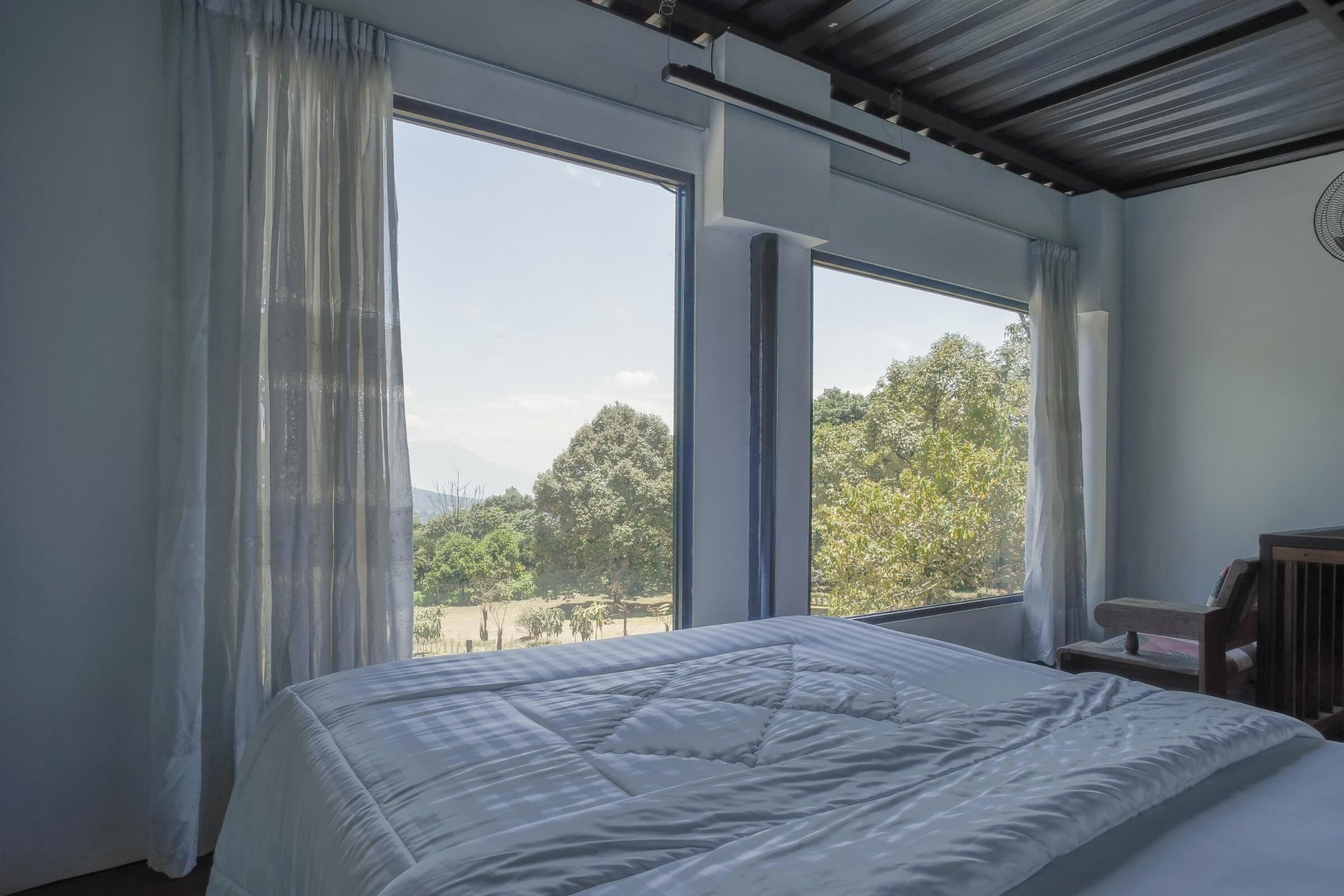 A bedroom with a large bed, a wooden headboard, and a view of trees through large windows.
