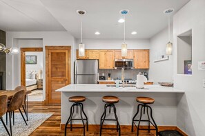 Una cocina moderna con armarios de madera, un refrigerador de acero inoxidable y una isla blanca con taburetes de bar.