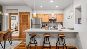 A modern kitchen with wooden cabinets, a stainless steel refrigerator, and a central island with bar stools.