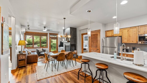 A modern kitchen with a large island, wooden cabinets, and a dining area with a sofa and chairs.