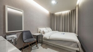 Habitación de hotel con cama, escritorio, silla, espejo y ventana con cortinas.