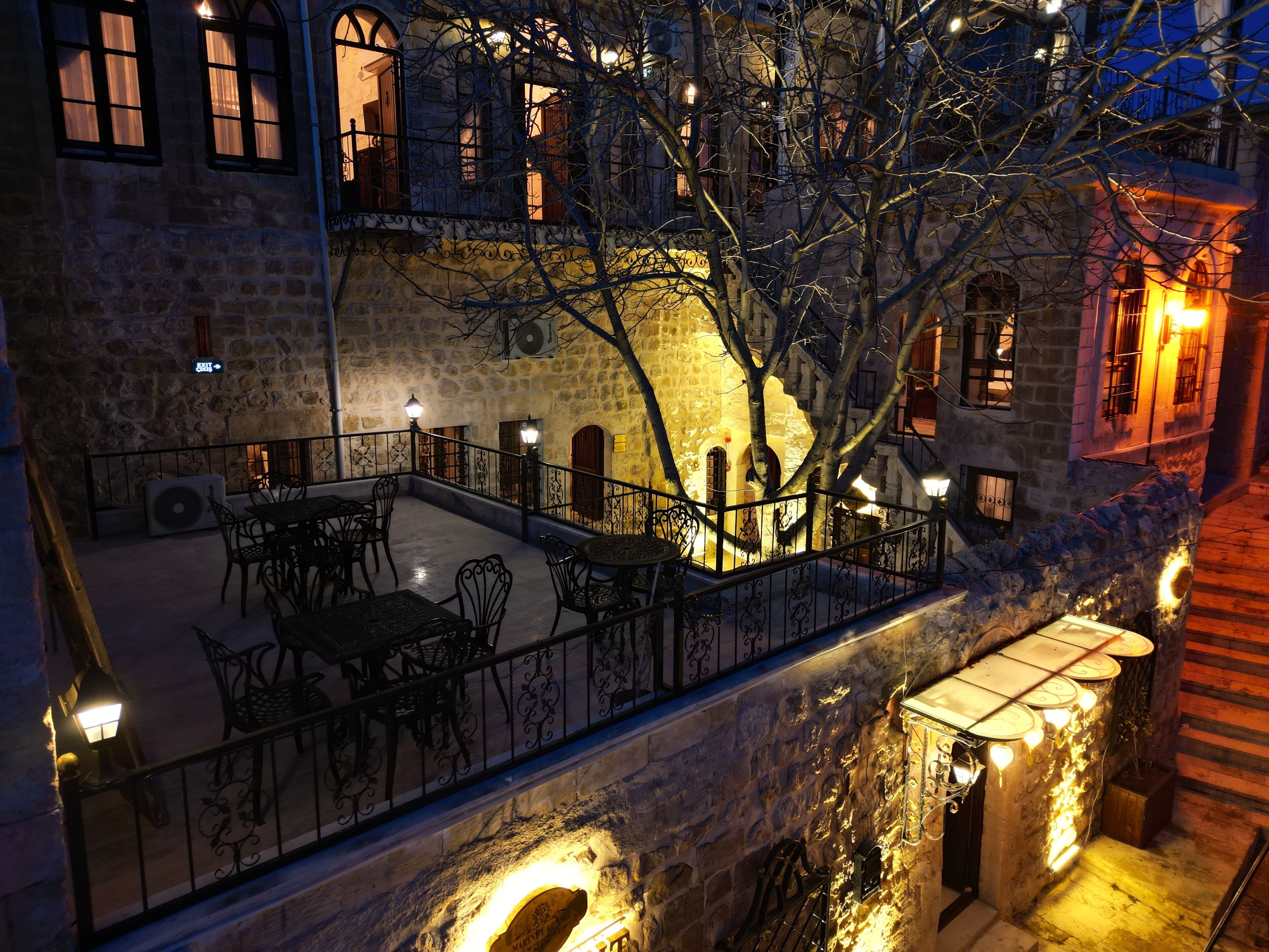 Ein steinerner Innenhof mit Außenbestuhlung, einer Treppe und Blick auf angrenzende Gebäude.