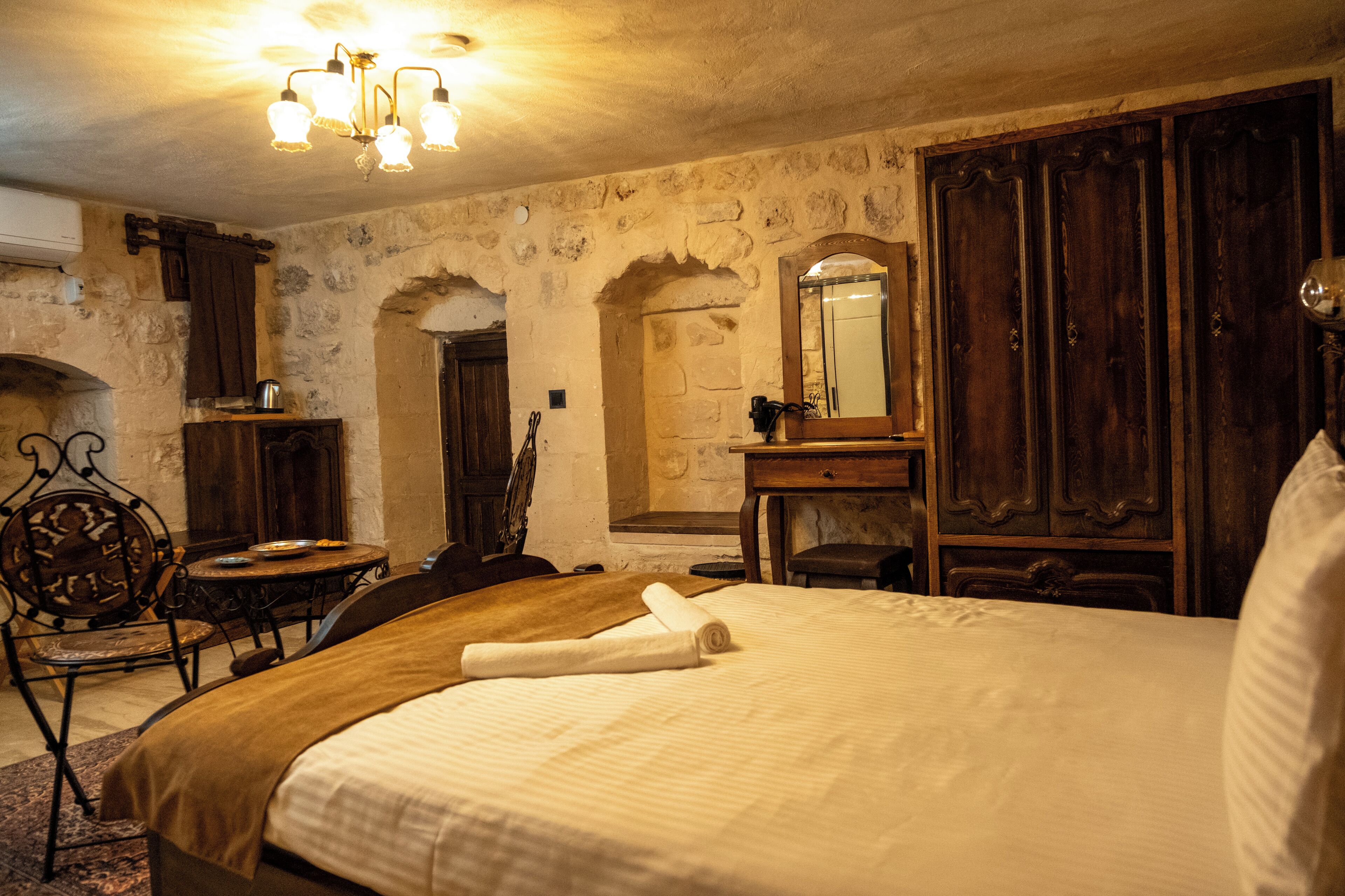 A bedroom with a large bed, wooden furniture, a stone wall, and a chandelier.