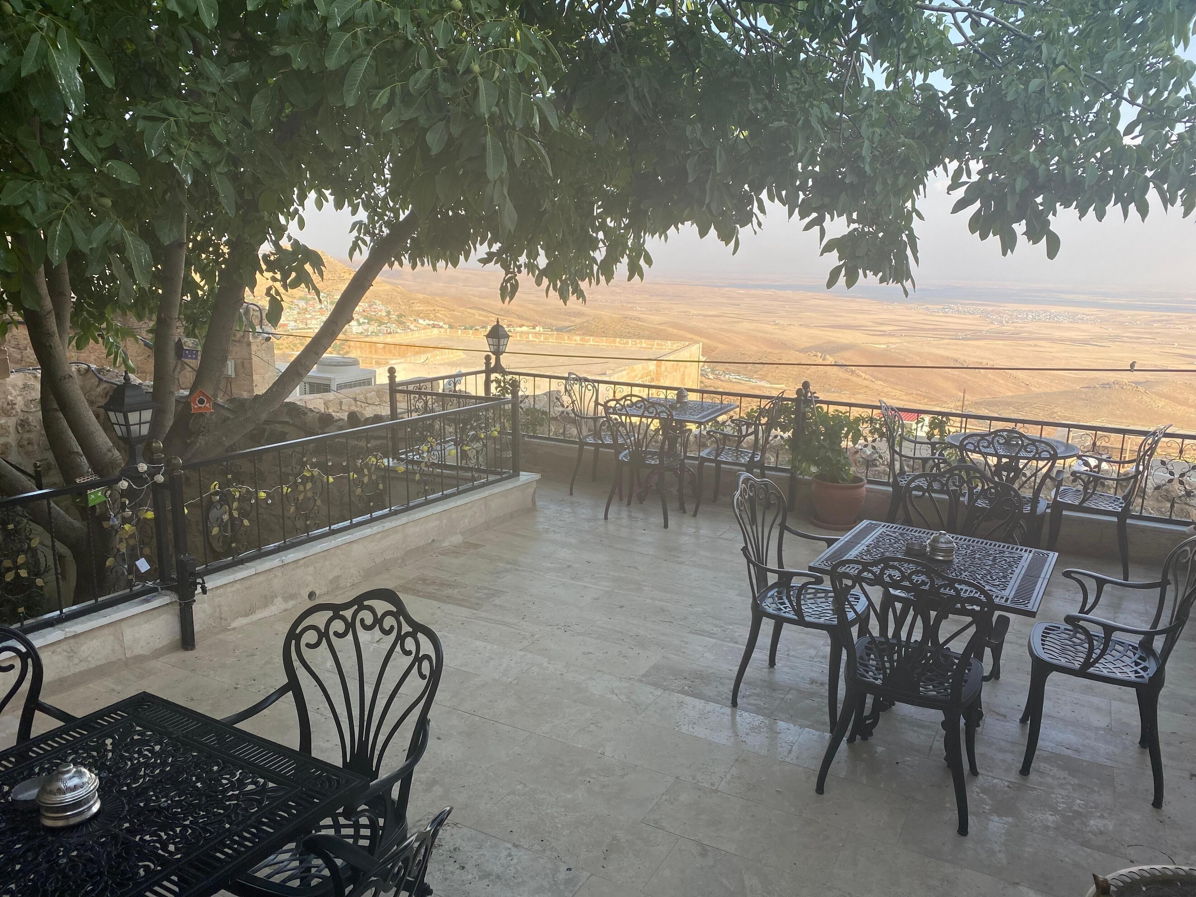 An outdoor seating area with tables and chairs, a railing, and a view of a distant landscape.