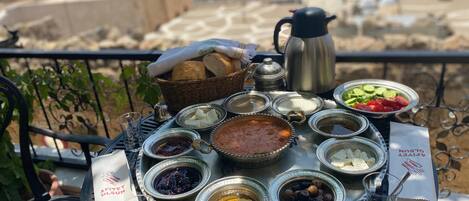 A table with various food items and a kettle, set on a balcony overlooking a scenic view.