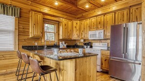 A wooden cabin-style kitchen with a central island, bar stools, a stainless steel refrigerator, and wooden cabinets.
