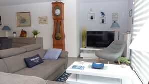 A living room with a sofa, a coffee table, a television, a clock, and decorative items on the wall.