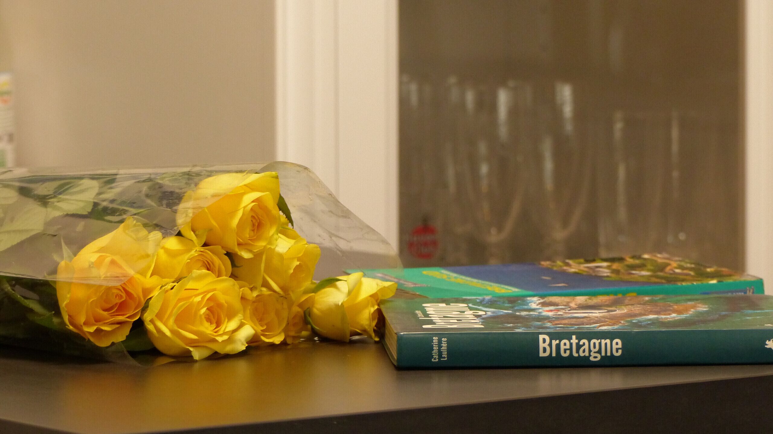 En bukett gula rosor och en bok med titeln ”Bretagne” ligger på ett bord.