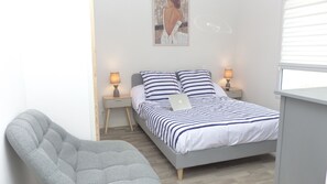 Een slaapkamer met een bed, twee bedlampen, een laptop, een grijze fauteuil en een schilderij aan de muur.