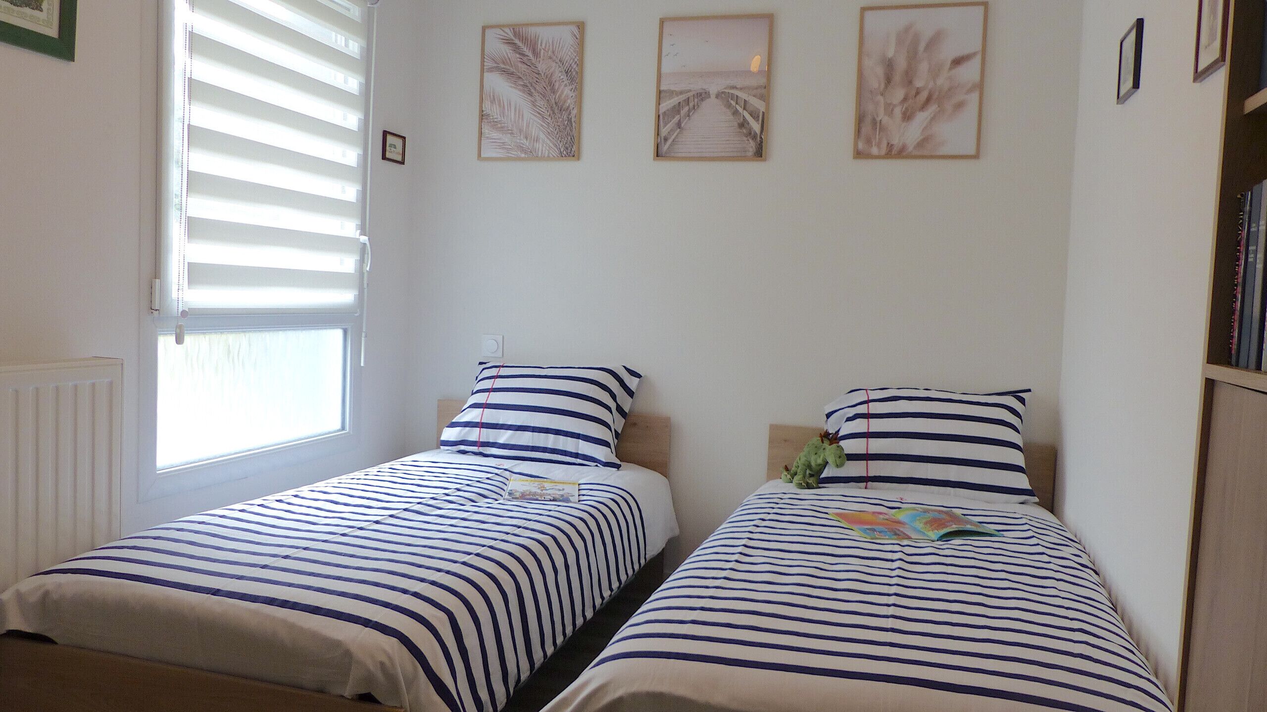 A bedroom with two single beds, each with striped bedding, a window with blinds, and wall art above the beds.