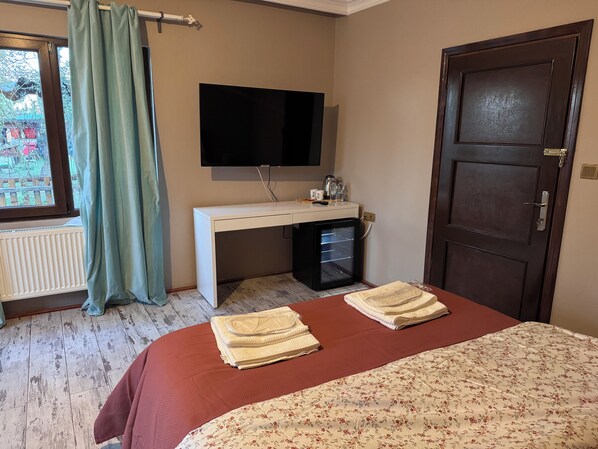 Un dormitorio con cama, escritorio, televisor, puerta y ventana con cortinas.