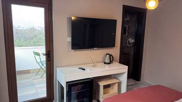 A room with a bed, a desk with a TV, a kettle, and a small fridge.