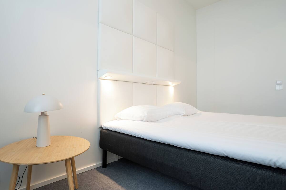 Une chambre à coucher moderne avec un lit, une table de chevet avec une lampe et un luminaire fixé au mur.