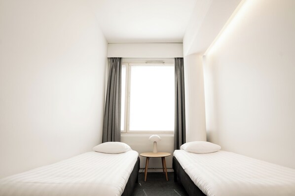 Een compacte, moderne hotelkamer met twee eenpersoonsbedden, een tafeltje en een raam met gordijnen.