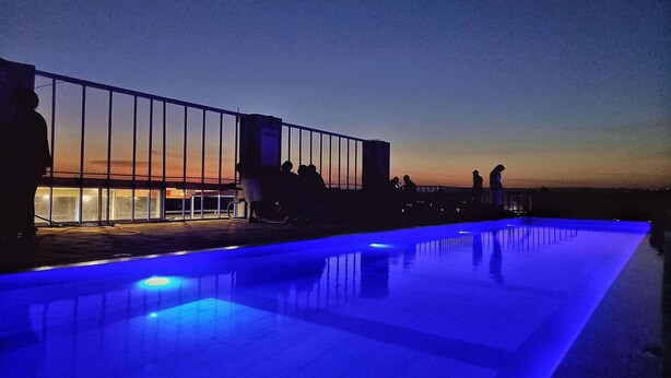 A rooftop pool with a glass barrier and people relaxing.