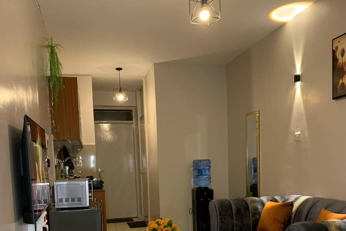 A hotel room with a bed, a sofa, a small table with a vase of flowers, a water dispenser, a television, and a microwave.