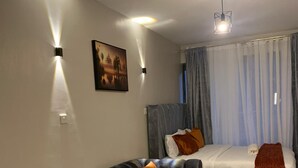 A modern living room with a sofa, a small round table with a vase, and a bed with curtains.