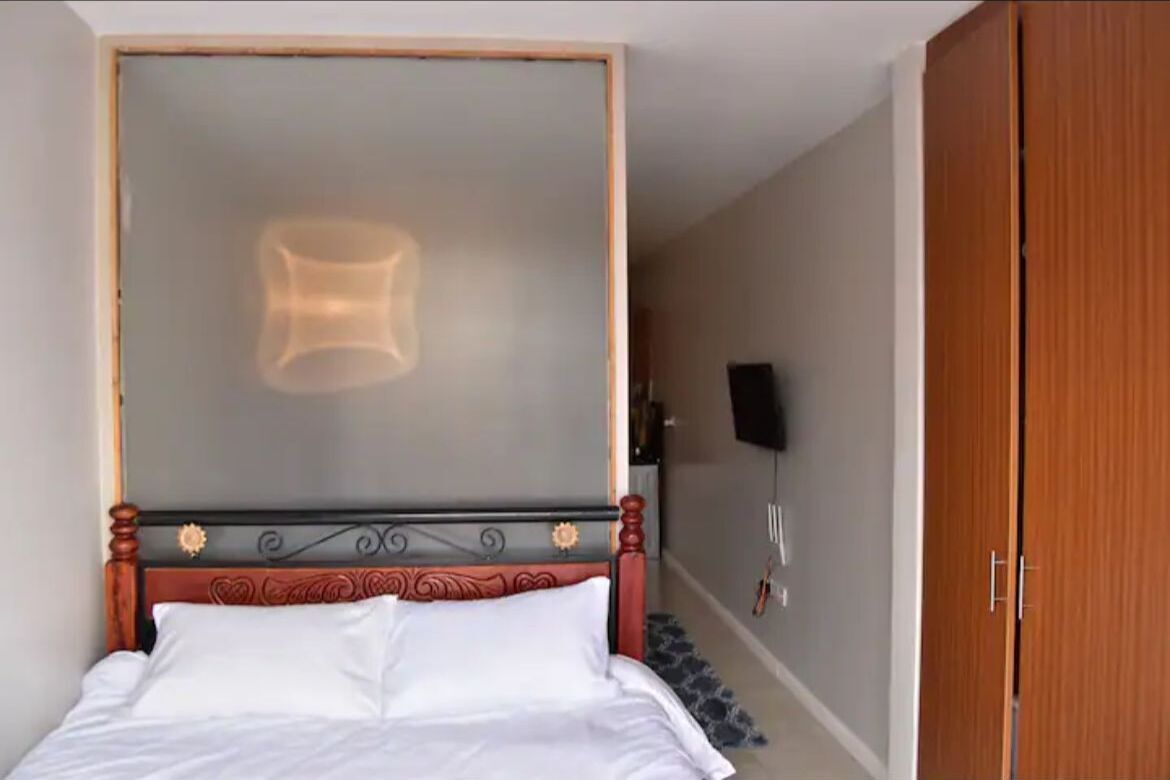 Un lit bien fait, avec une tête de lit en bois, un luminaire fixé au mur et une armoire en bois.
