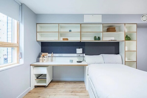 A compact bedroom with a bed, a desk, and built-in shelving.