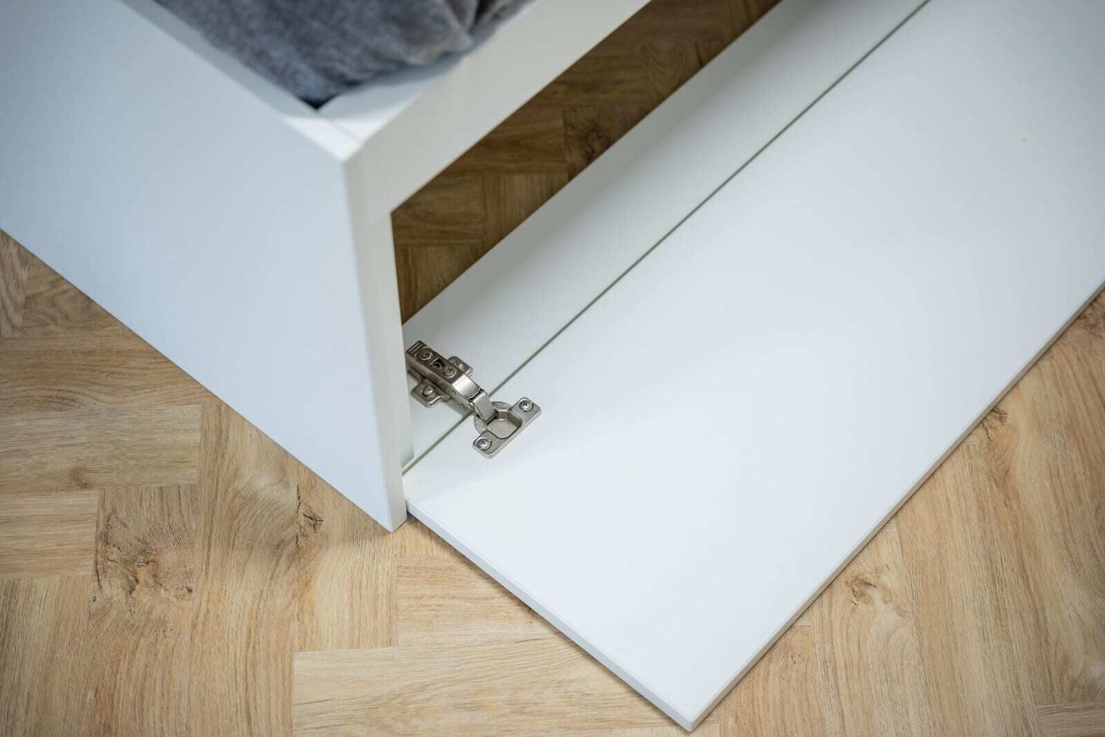 Un mueble blanco con una puerta abatible entreabierta, mostrando un suelo de madera debajo.