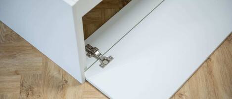 Un mueble blanco con una puerta abatible entreabierta, mostrando un suelo de madera debajo.