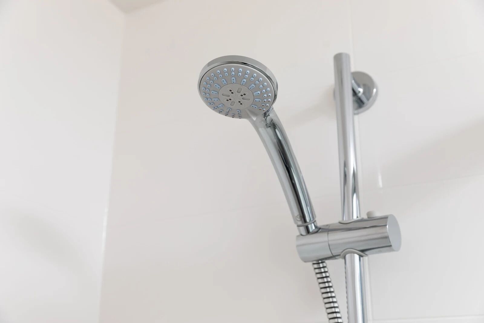 Une pomme de douche chromée, dotée d’un flexible et fixée au mur.